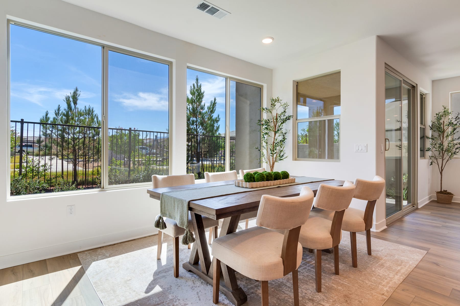 A modern and spacious dining room with large windows overlooking a scenic outdoor landscape featuring pine trees and a clear sky.