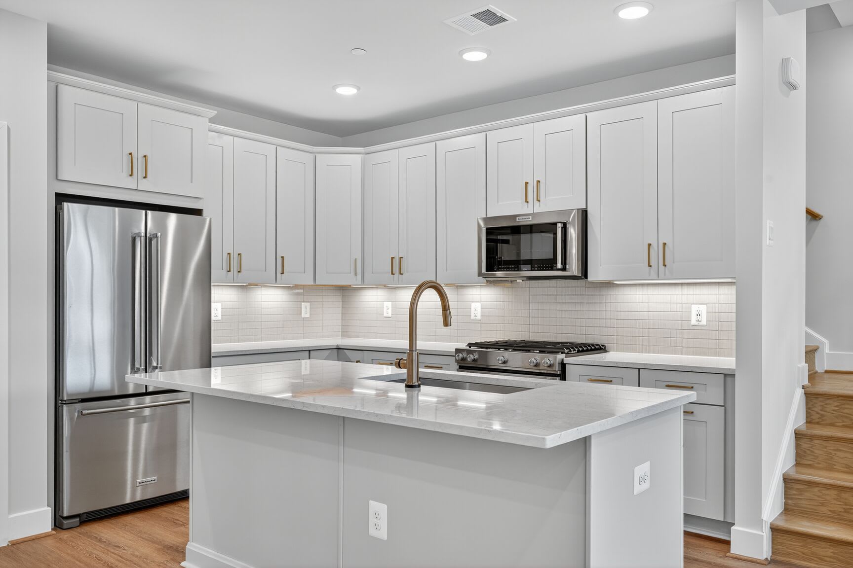 A modern, well-equipped kitchen with white cabinets, stainless steel appliances, and a central island with a quartz countertop.