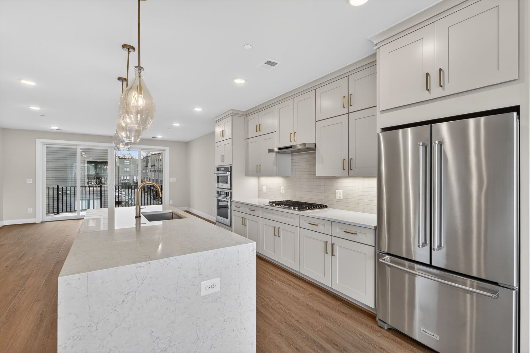 A modern, well-equipped kitchen with white cabinets, stainless steel appliances, and a large central island with a marble countertop.