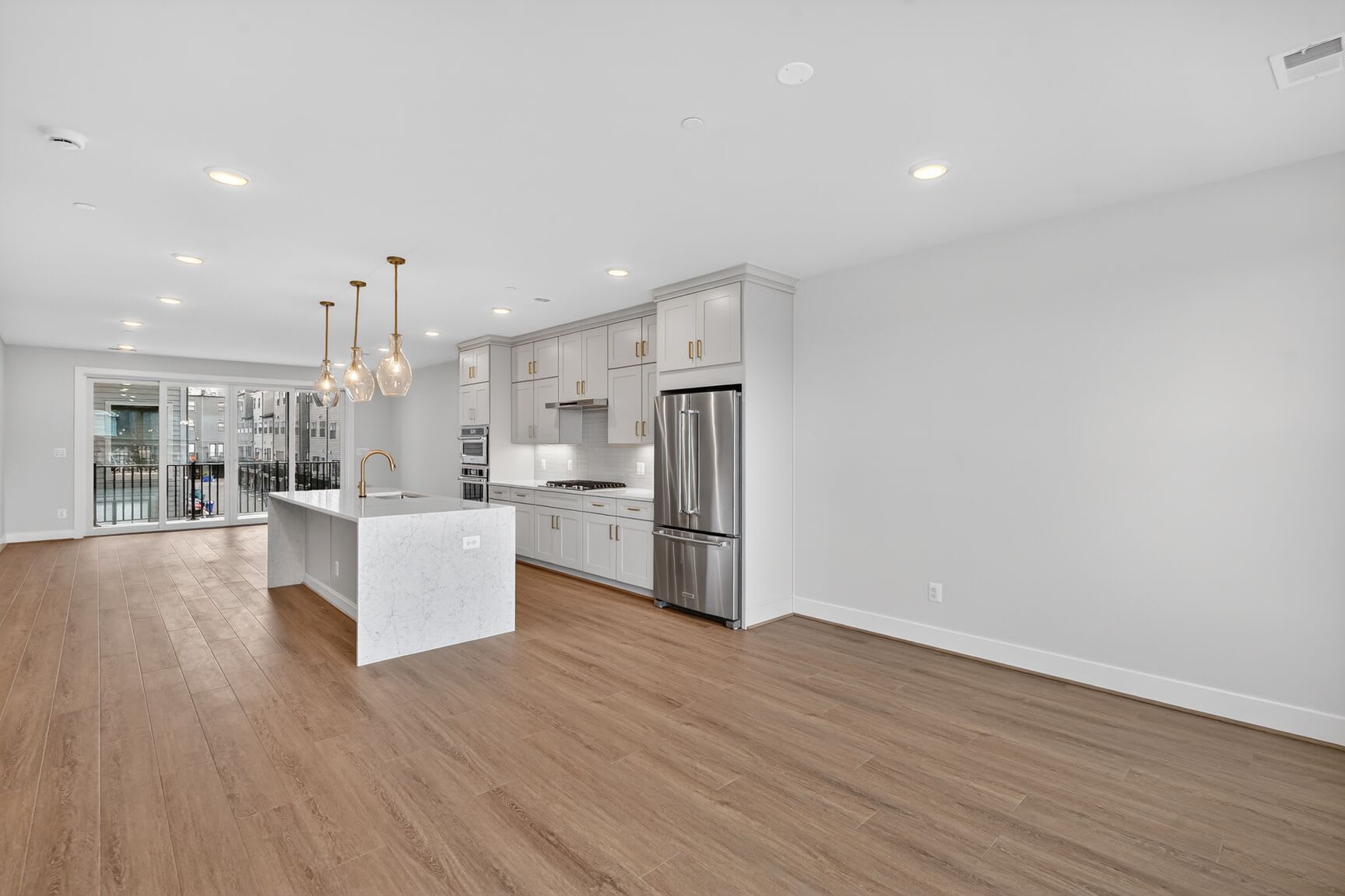 A modern, open-concept kitchen with white cabinets, stainless steel appliances, and a wooden floor extends into a bright, airy living space.