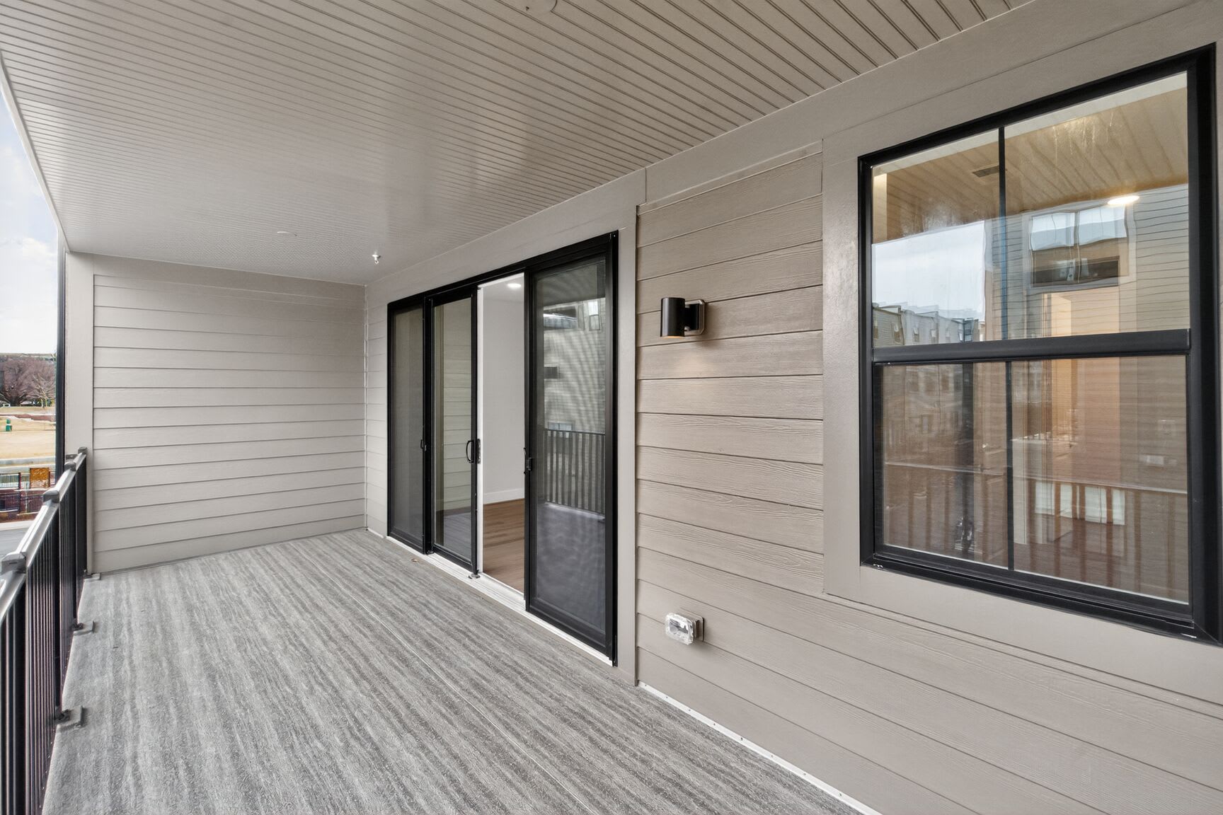 A spacious and well-lit balcony or patio with a wooden floor, white walls, and large sliding glass doors that provide a view of the exterior.