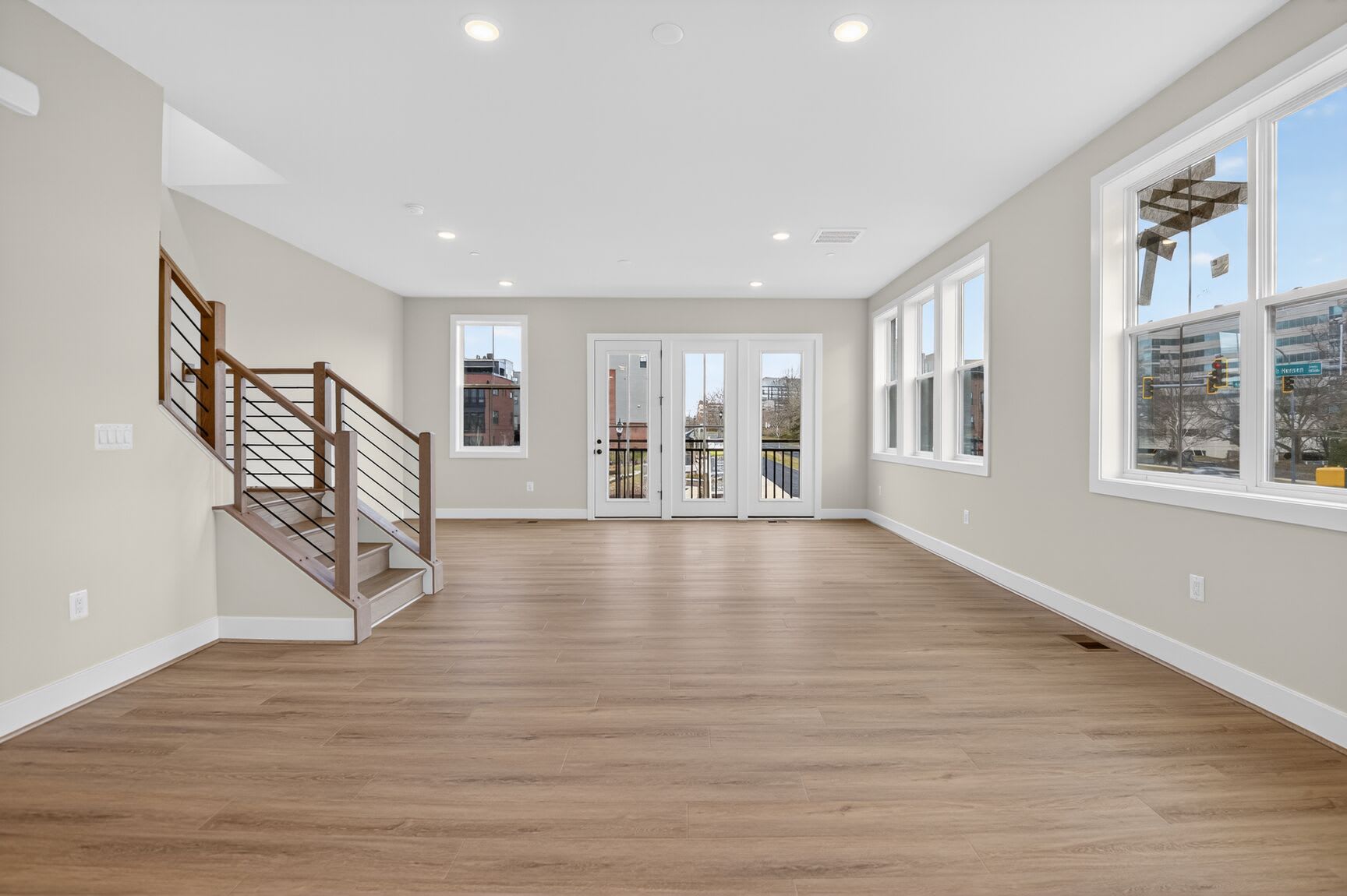 A spacious and bright interior with hardwood floors, a staircase, and large windows providing natural light.
