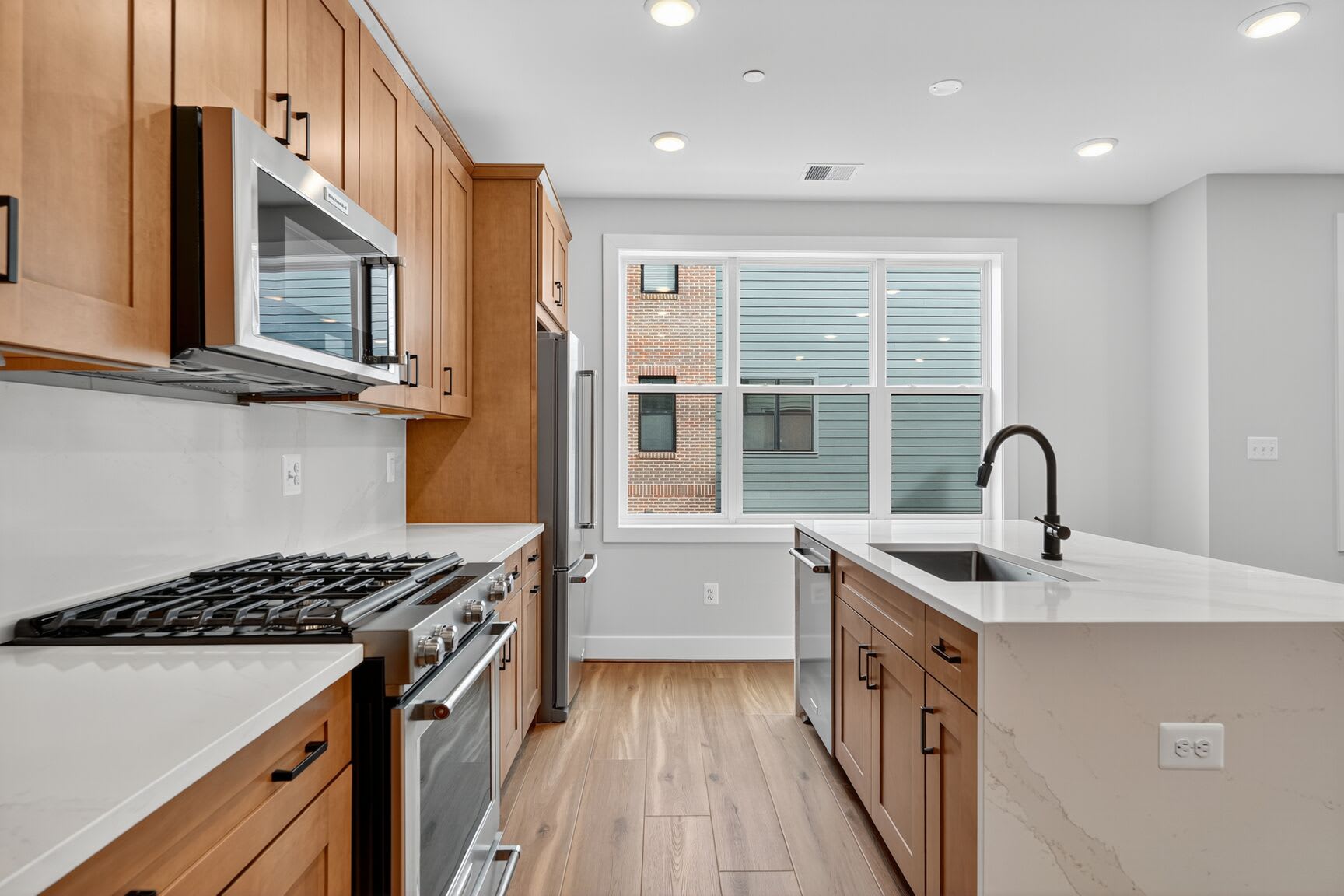 A modern, well-lit kitchen with wooden cabinets, stainless steel appliances, and a large window providing natural light.