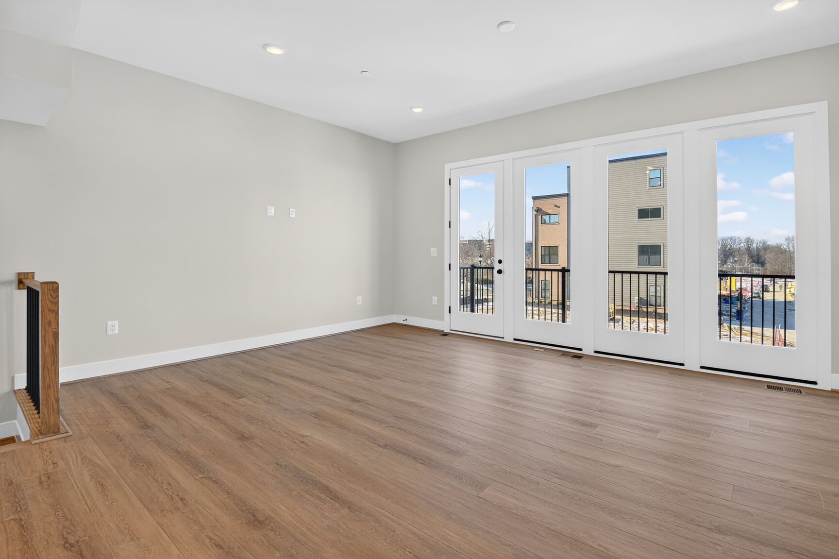 A spacious, well-lit room with hardwood floors, white walls, and large windows overlooking a scenic outdoor view.