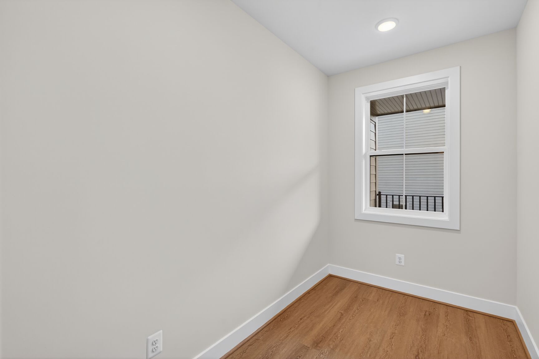 A bright, empty room with a window and hardwood flooring, providing a clean and minimalist space.