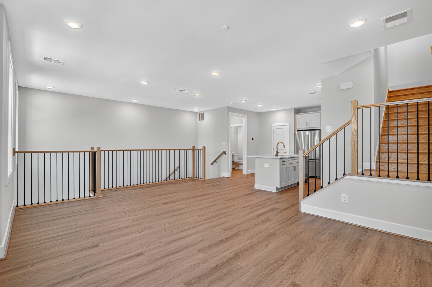 A spacious, open-concept interior with hardwood floors, white walls, and a staircase with metal railings leading to an upper level.