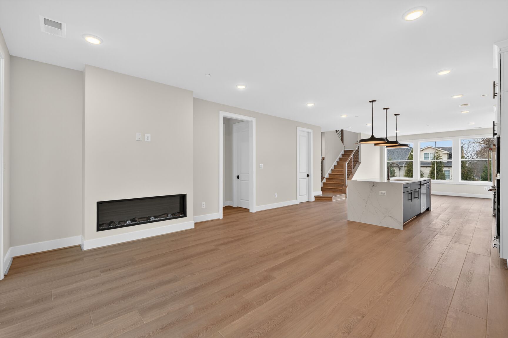 A spacious and modern open-concept living area with a fireplace, hardwood floors, and a kitchen visible in the background.