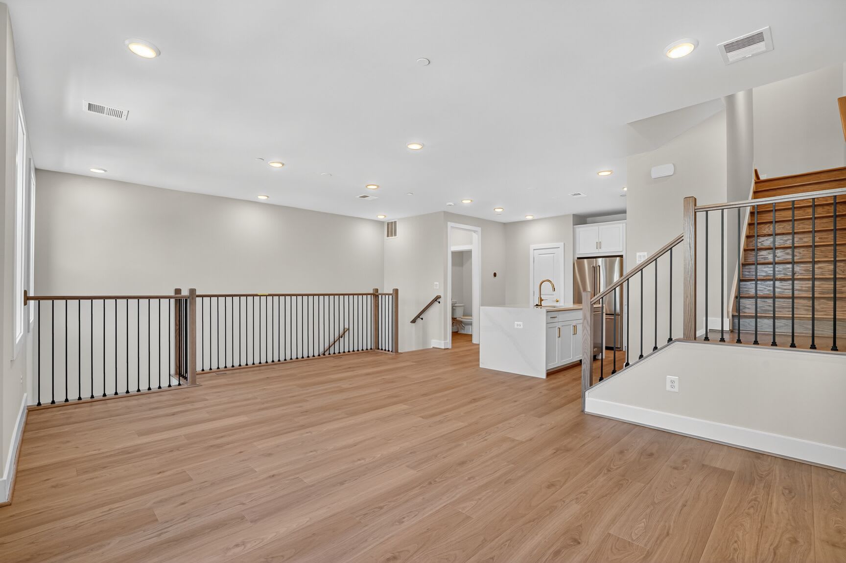 A spacious, open-concept interior with hardwood floors, a staircase with metal railings, and a bright, airy atmosphere.