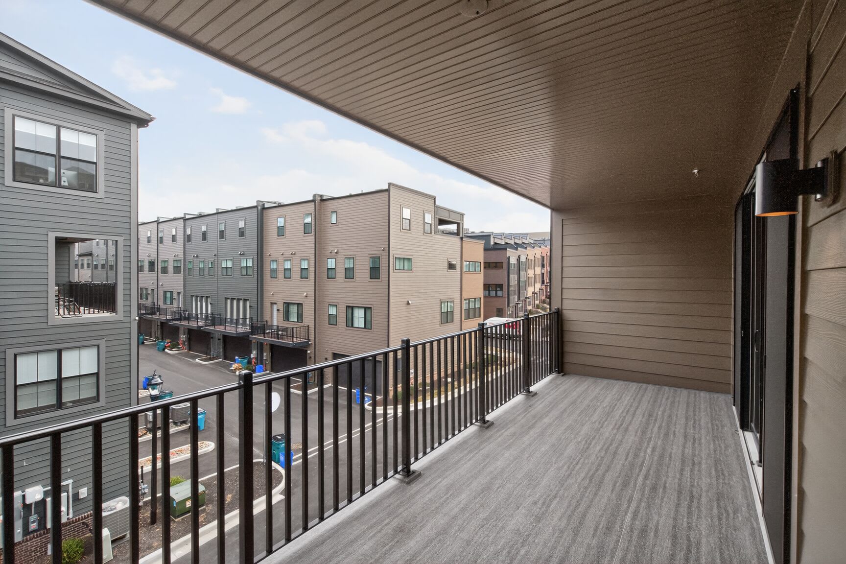 A balcony with a wooden floor and metal railing overlooks a residential neighborhood with multi-story buildings in the background.