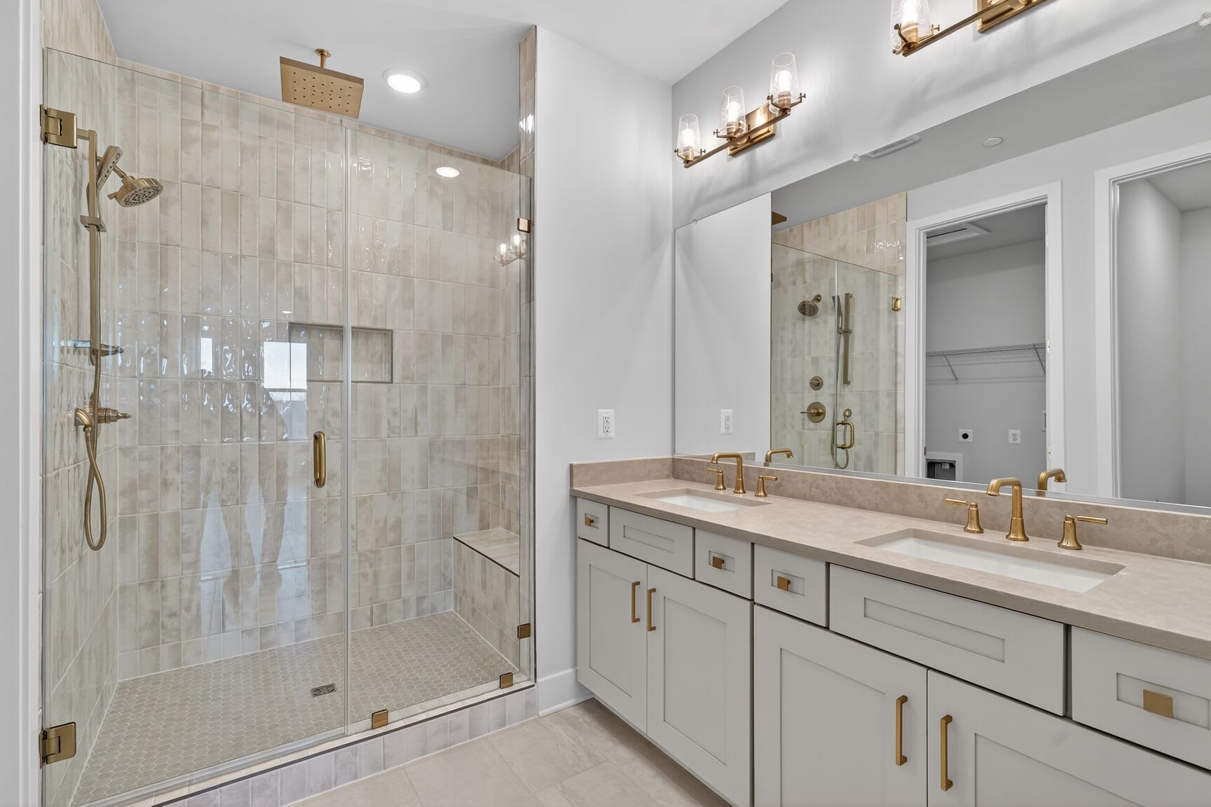 A modern and spacious bathroom with a large glass shower enclosure, a double vanity with a marble countertop, and brass fixtures, all set against a neutral color palette.