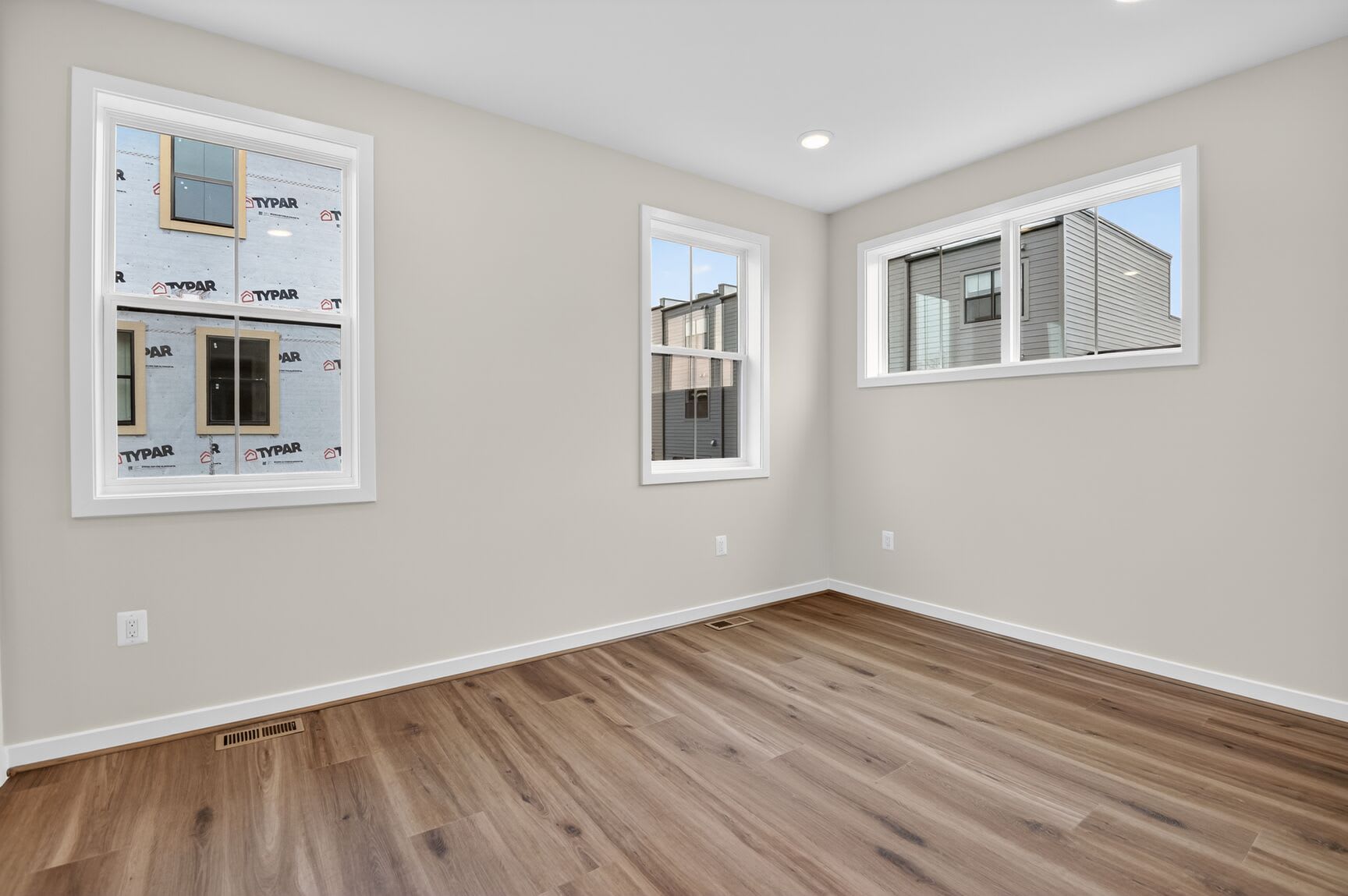 A spacious, well-lit room with a wooden floor and a framed poster on the wall, overlooking a neighboring building through a window.