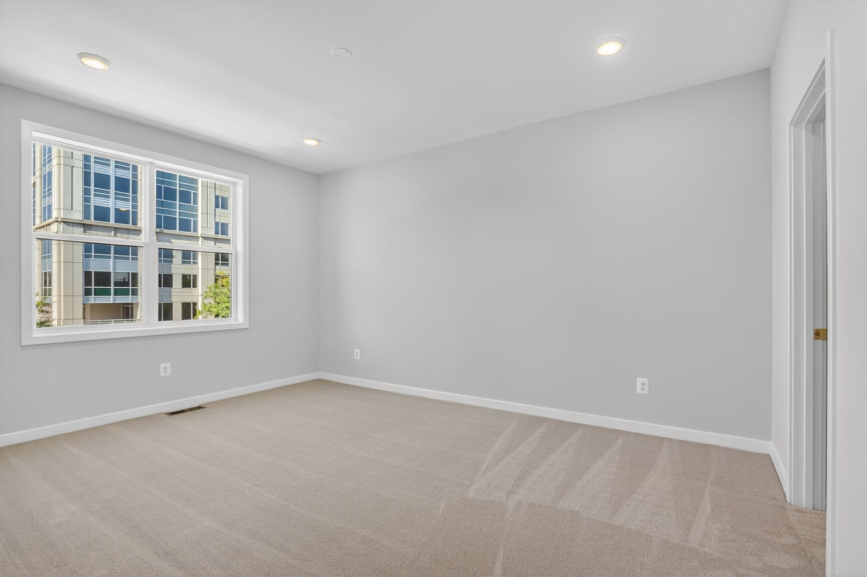 A spacious, well-lit room with large windows, hardwood floors, and a neutral color scheme.