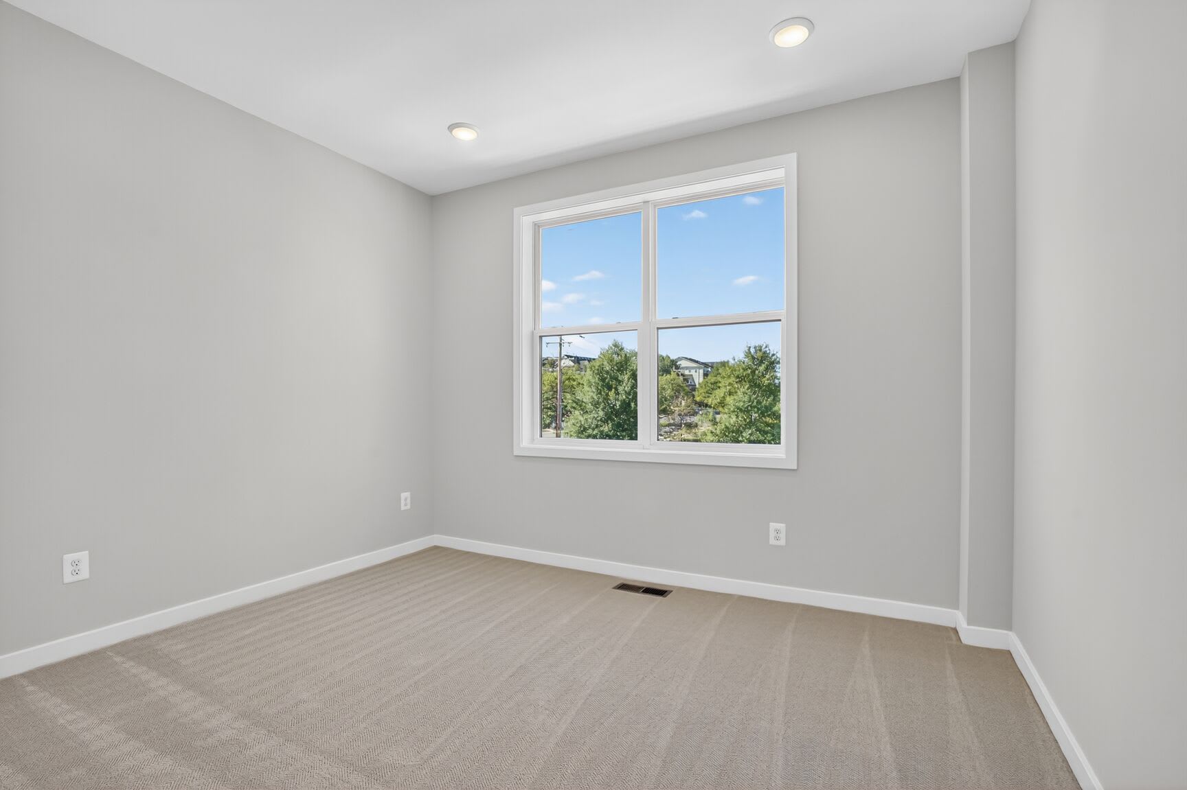 A spacious, well-lit room with a large window overlooking a lush, green outdoor landscape.