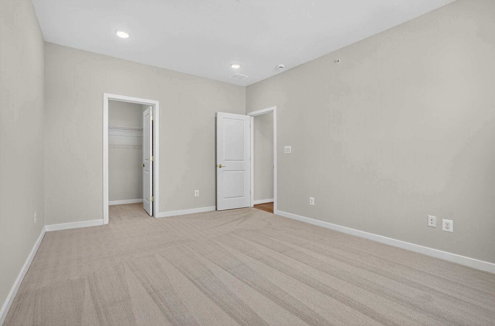 A spacious, minimalist room with light-colored walls, hardwood flooring, and two white doors leading to other areas.