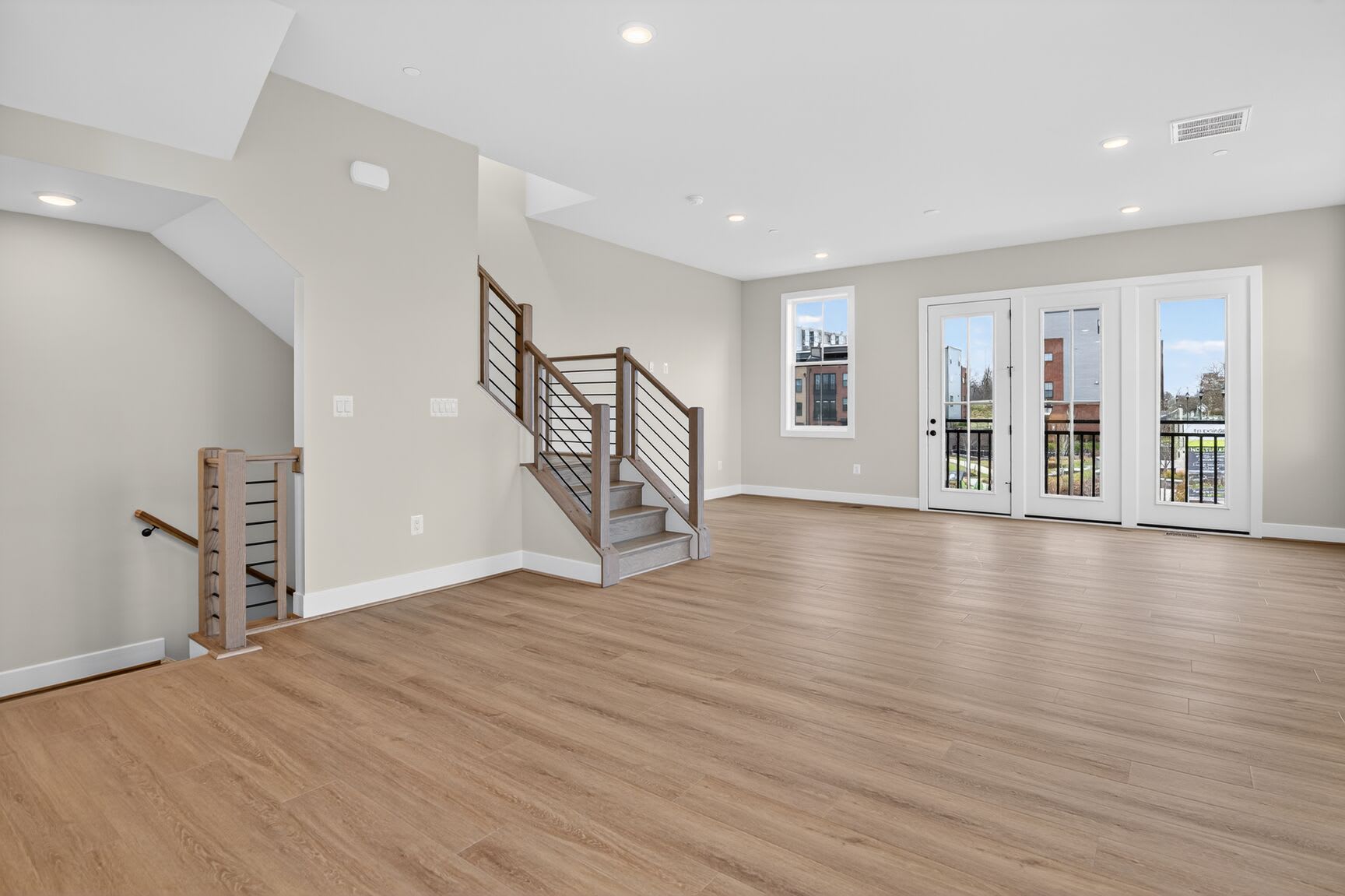 A spacious, modern living room with hardwood floors, a staircase, and large windows providing ample natural light.