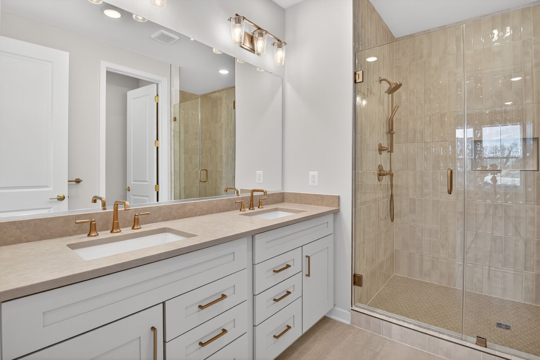 A modern and spacious bathroom with a double vanity, a large mirror, and a glass-enclosed shower area, all featuring a neutral color palette and sleek, contemporary design.