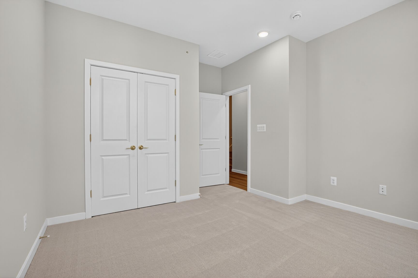 A spacious, minimalist room with white doors, light-colored walls, and a hardwood floor.
