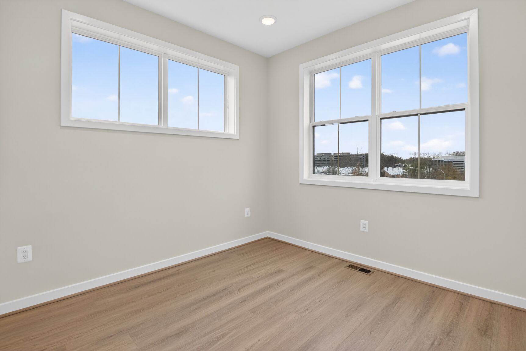 A bright and spacious room with large windows overlooking a scenic outdoor view, featuring a hardwood floor and neutral-colored walls.