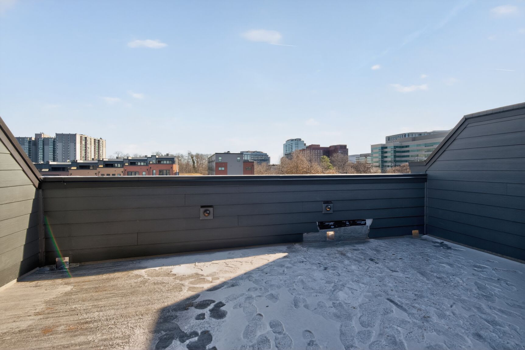 A snowy outdoor balcony or terrace overlooking a cityscape with tall buildings in the background.