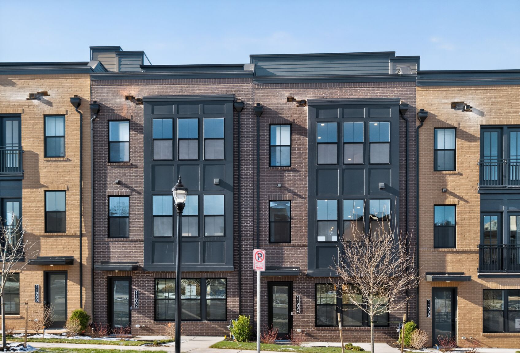 A multi-story brick building with large windows and a modern architectural design, surrounded by bare trees and a clear blue sky.