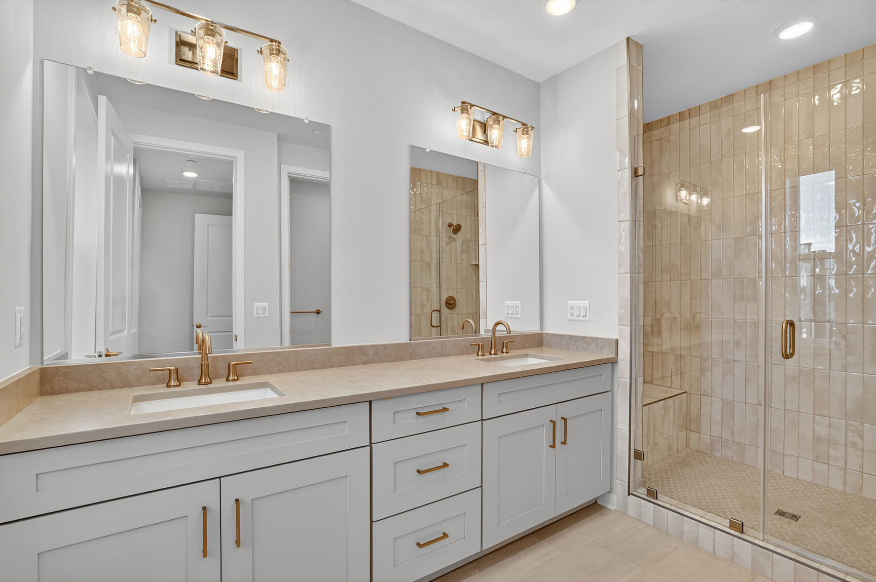 A modern and spacious bathroom with a large vanity, double sinks, and a glass-enclosed shower area, featuring a neutral color palette and warm lighting.