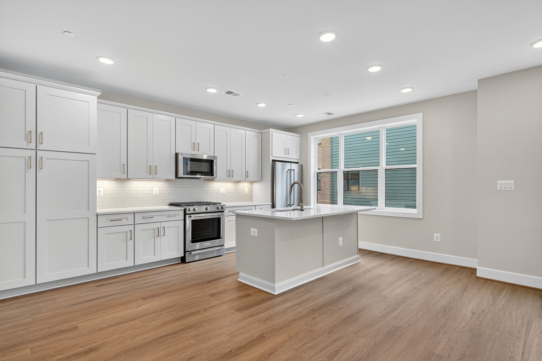 A modern, well-lit kitchen with white cabinets, stainless steel appliances, and a central island with a wooden countertop, set against a backdrop of hardwood floors.