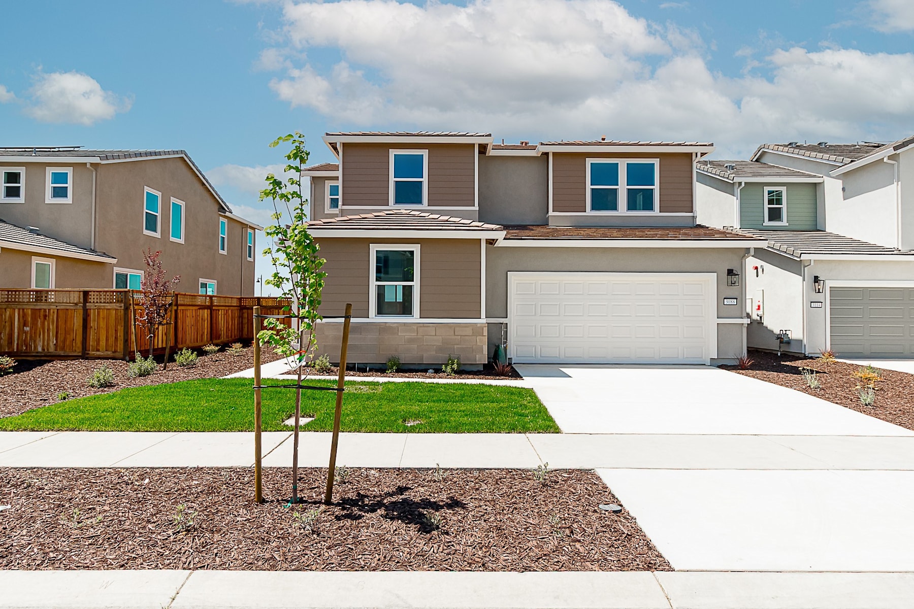 A modern two-story residential home with a well-maintained lawn, surrounded by other similar houses in a suburban neighborhood.