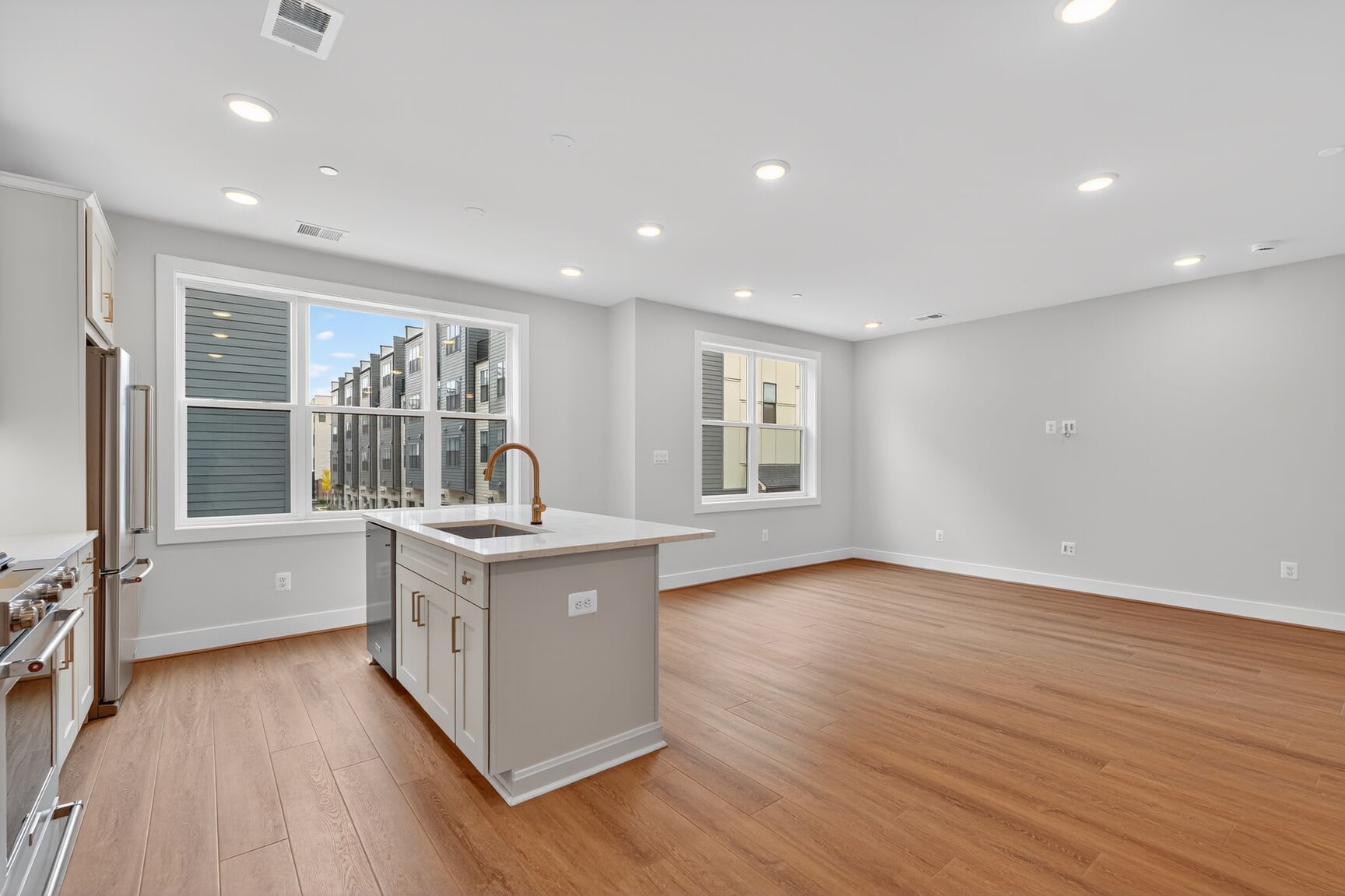 A modern, open-concept kitchen with white cabinets, hardwood floors, and large windows providing ample natural light.