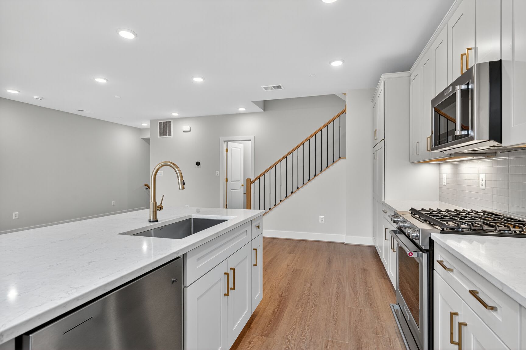 A modern, open-concept kitchen with white cabinets, stainless steel appliances, and a wooden staircase leading to the upper level.