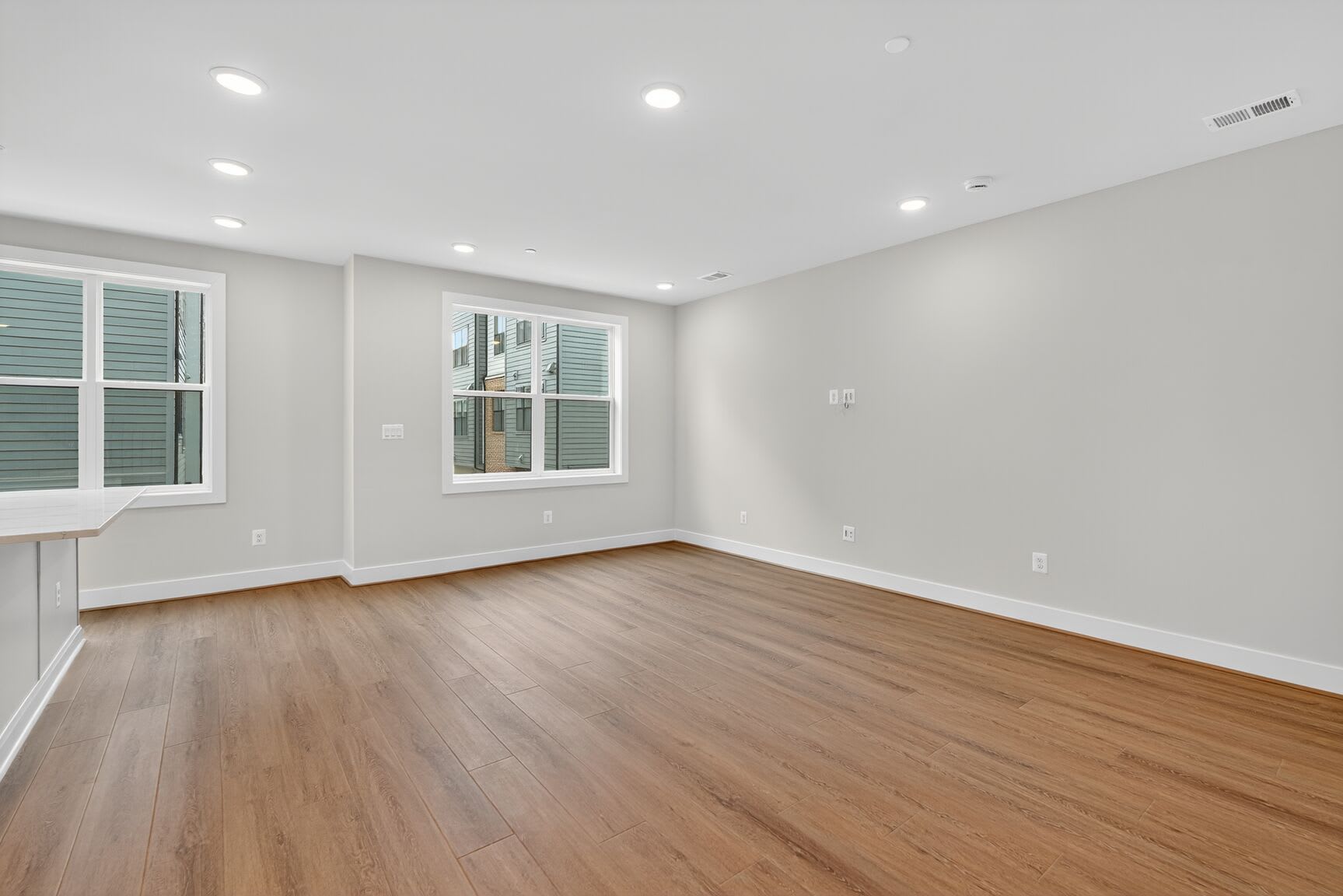 A spacious, well-lit room with hardwood floors, white walls, and recessed lighting fixtures.