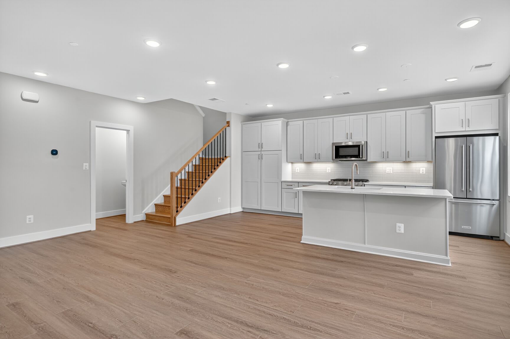 A modern, open-concept kitchen and living space with white cabinets, hardwood floors, and a staircase leading to an upper level.
