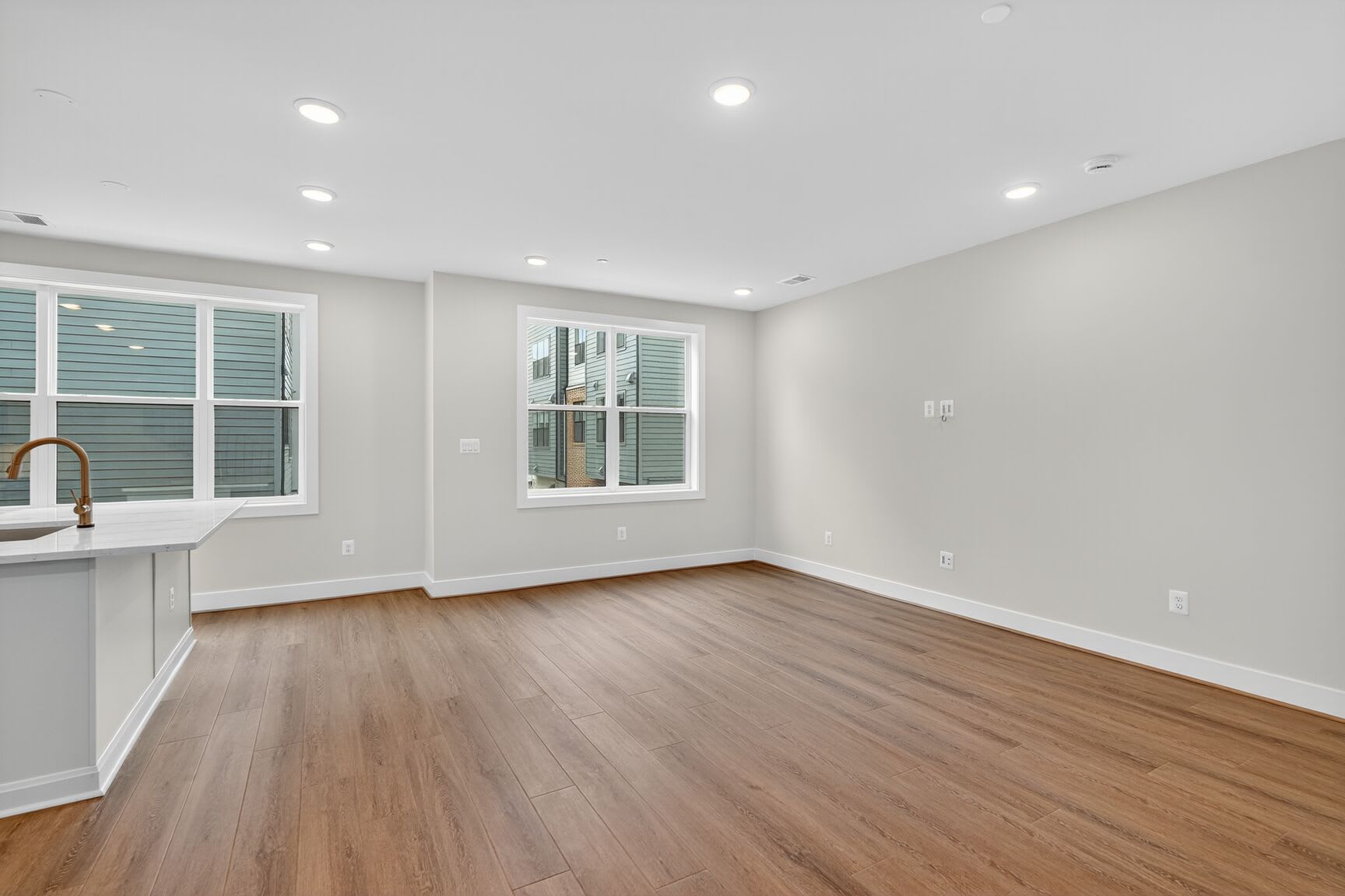 A bright and spacious room with hardwood floors, white walls, and recessed lighting, featuring a kitchen area with a sink and countertop.