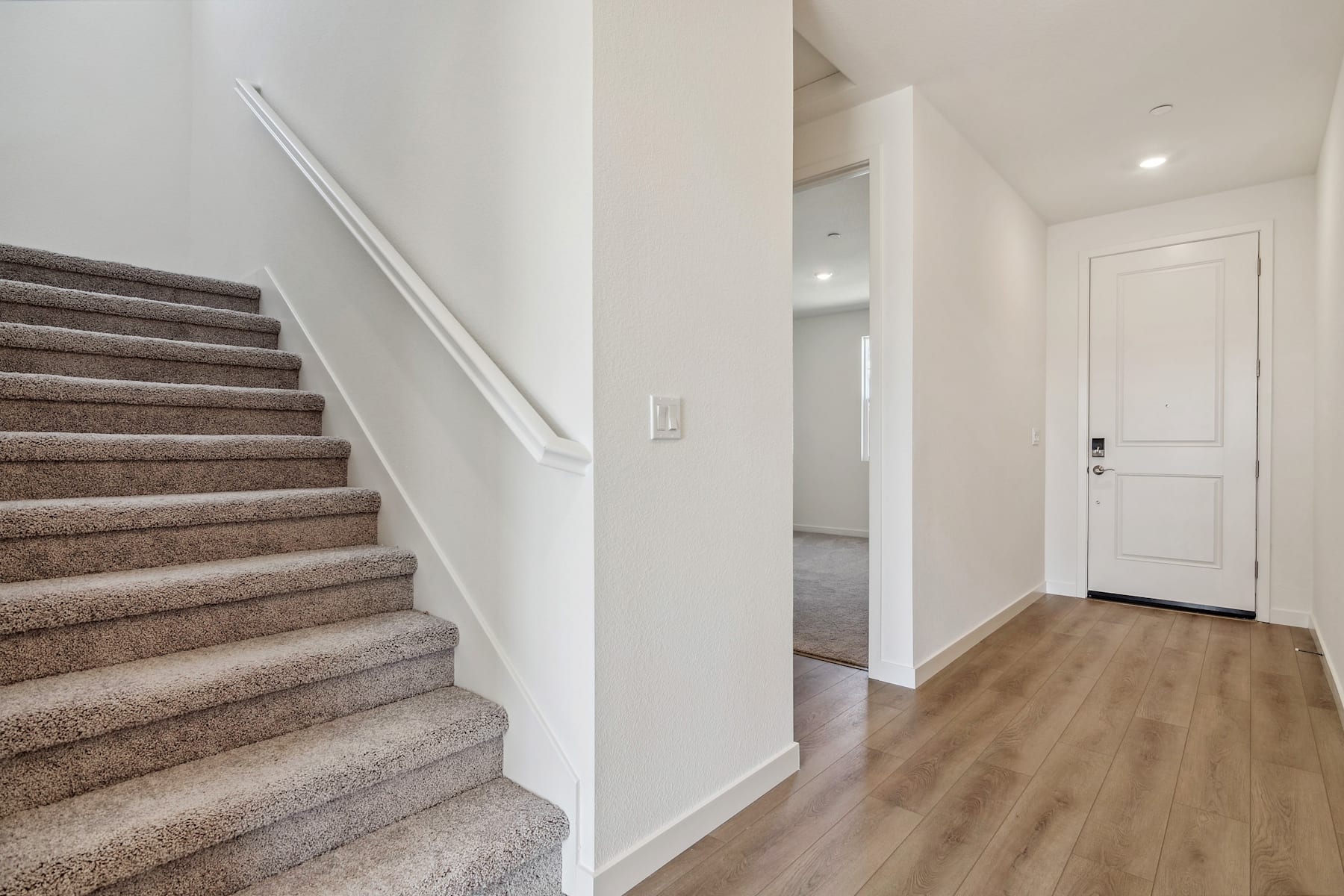 A carpeted staircase leads up to a hallway with a white door, and the floor is covered in light-colored wood paneling.