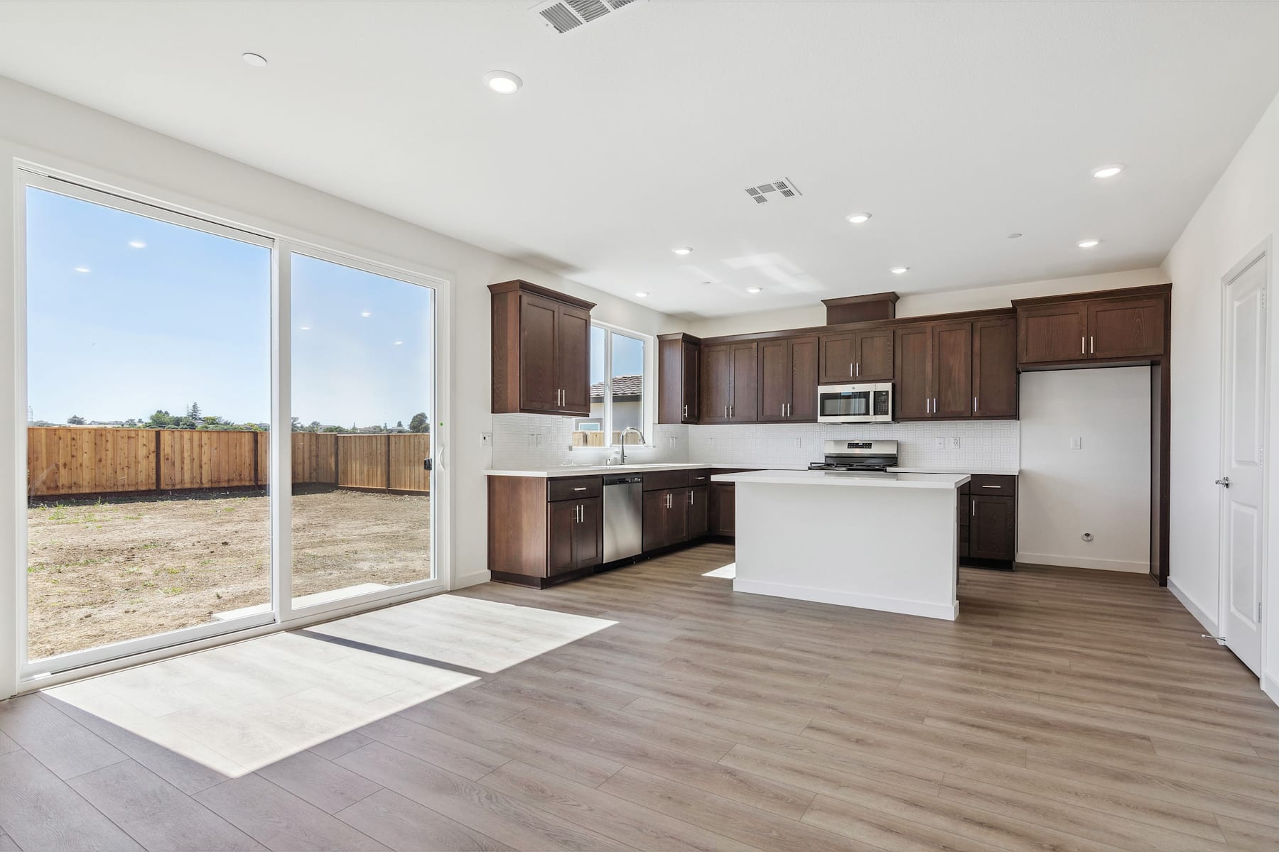 A modern, open-concept kitchen and living space with large windows overlooking a fenced backyard.