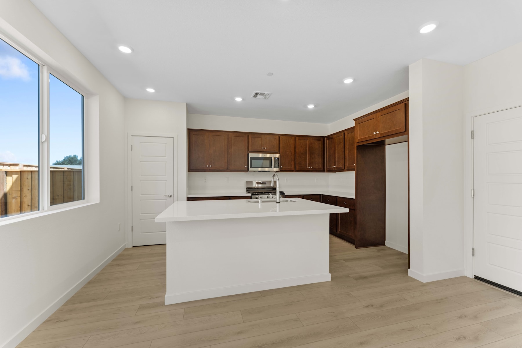 A modern, open-concept kitchen with white countertops, wooden cabinets, and a large window providing natural light.