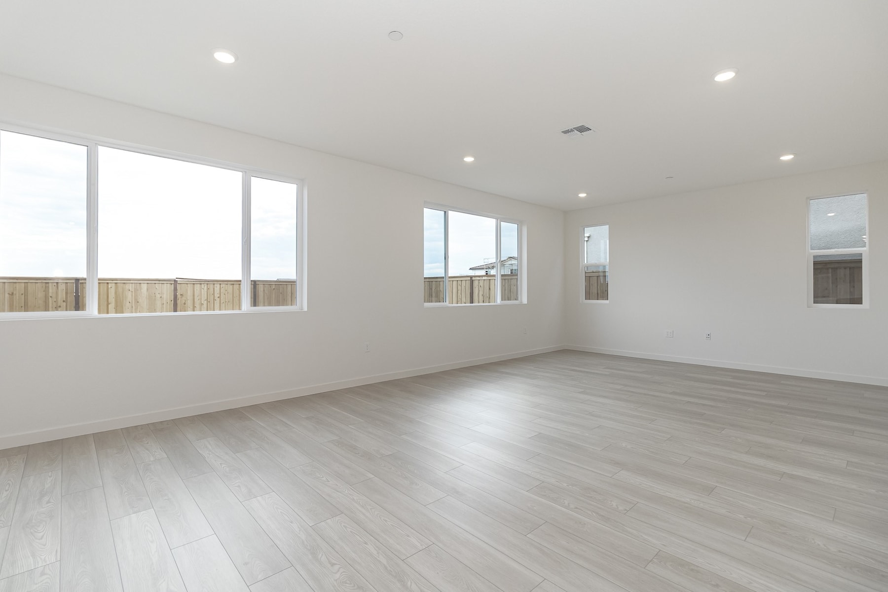 A spacious, well-lit room with clean, white walls and a hardwood floor. Large windows along the walls provide ample natural light, creating a bright and airy atmosphere.