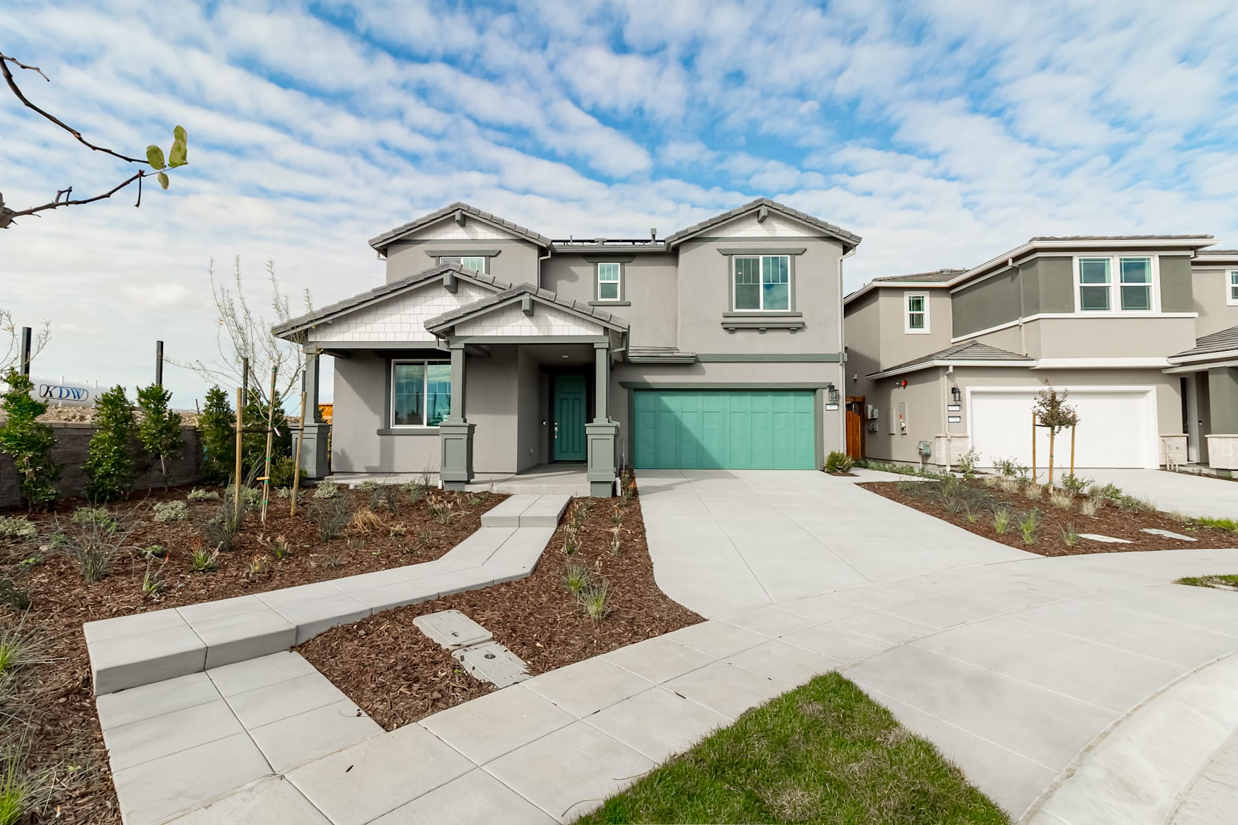 A modern two-story residential house with a gray exterior, a green garage door, and a well-landscaped front yard with a concrete walkway leading to the entrance.