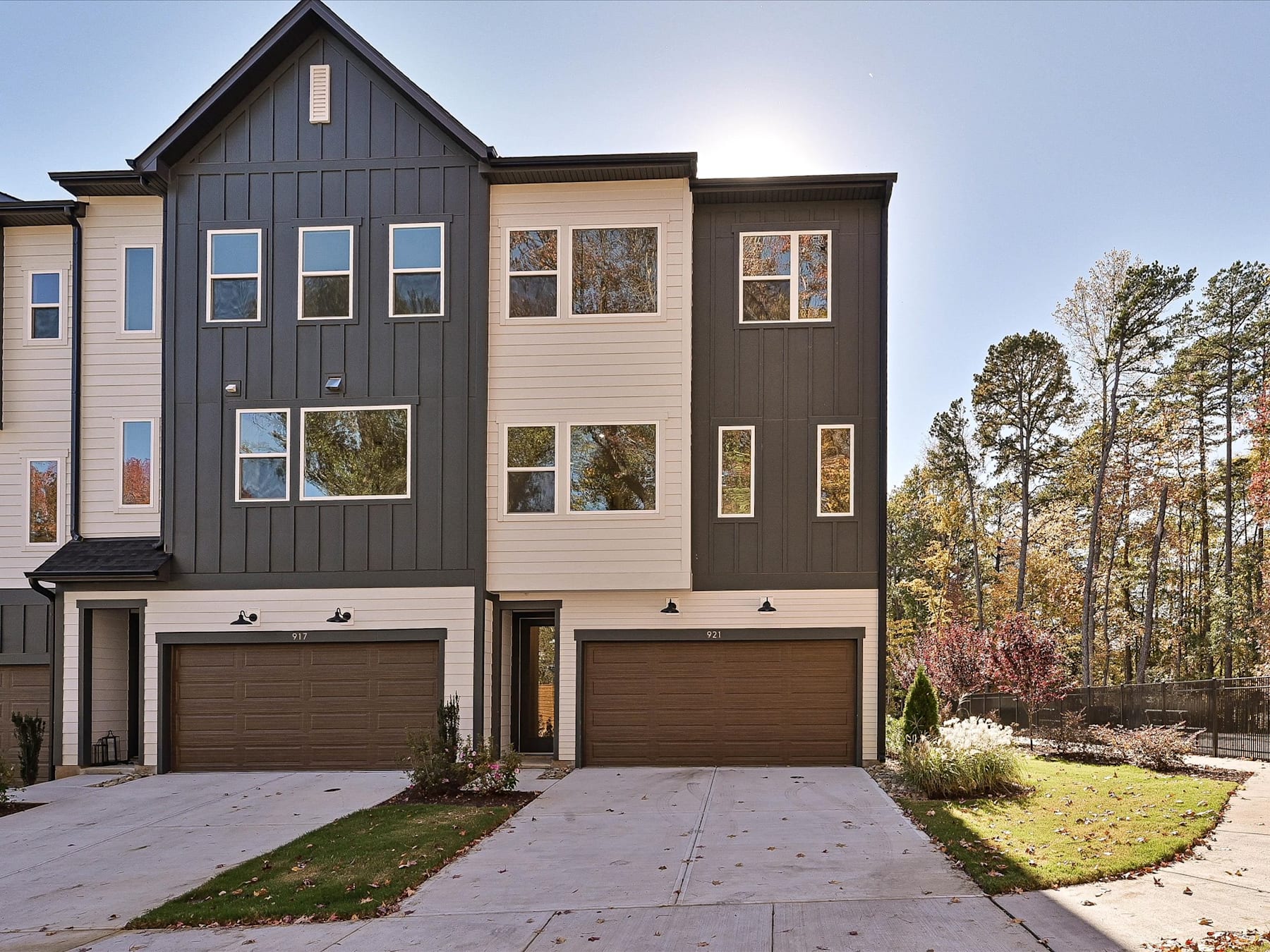 A modern, two-story townhouse with a mix of gray and beige siding, surrounded by a grassy yard and pine trees in the background.