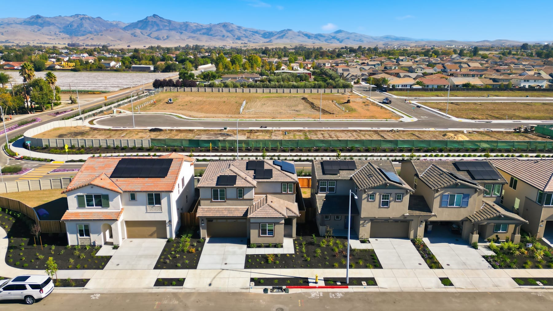 A residential neighborhood with rows of townhouses in the foreground, surrounded by a lush green landscape and a backdrop of majestic mountains in the distance.