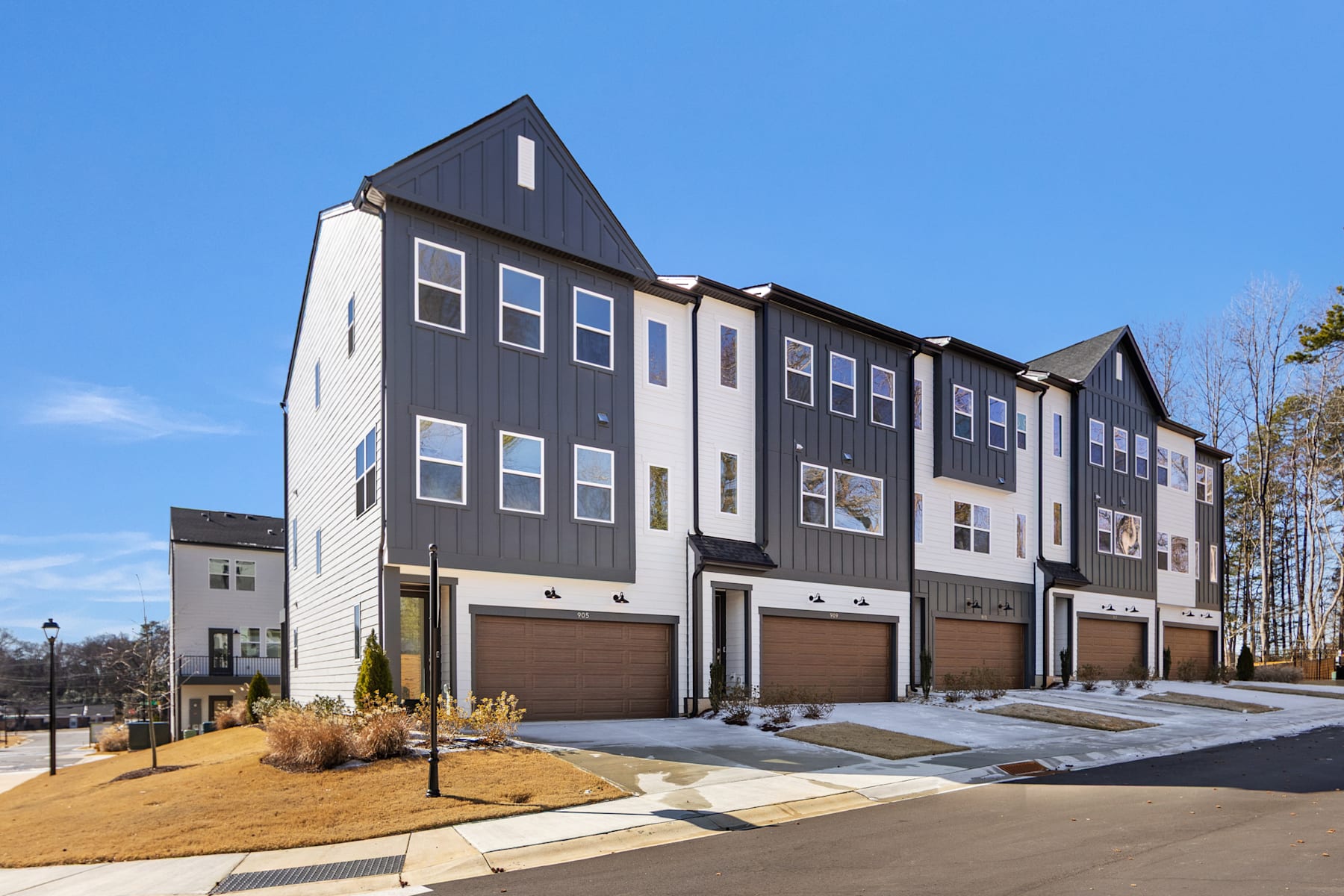 A modern multi-story townhouse complex with a mix of gray and white siding, set against a clear blue sky and surrounded by a paved driveway and landscaped grounds.