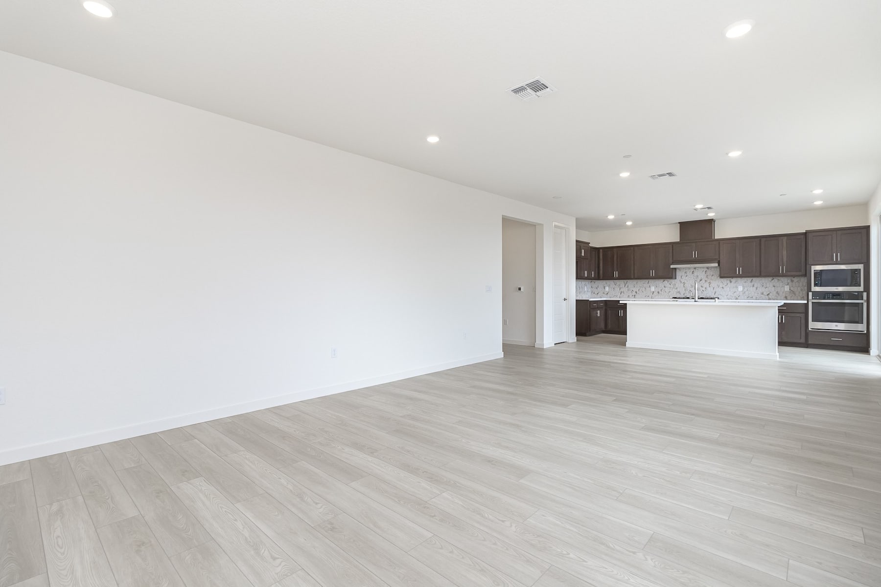A spacious, open-concept living area with a modern kitchen and hardwood flooring, featuring a clean and minimalist design.