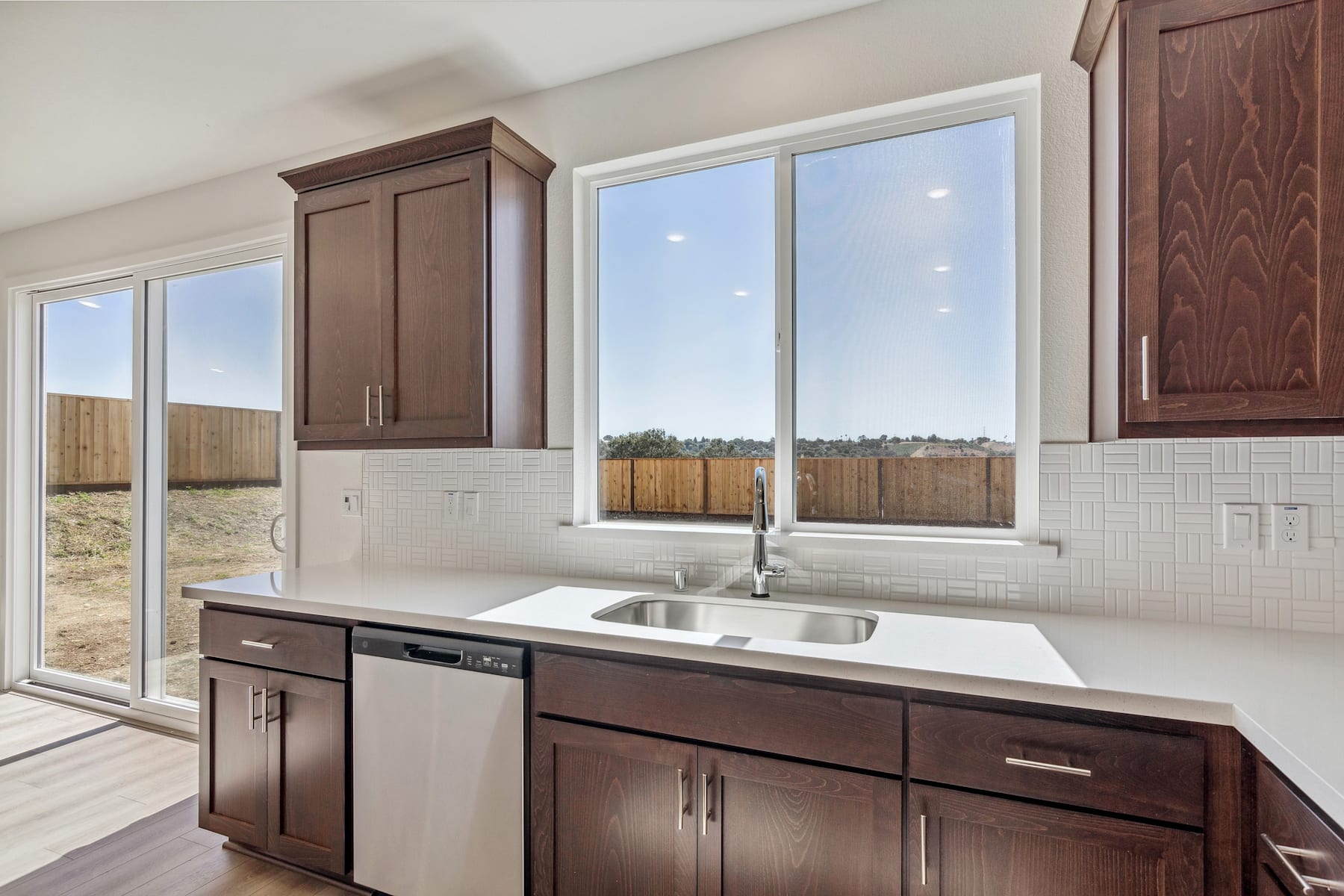 A modern kitchen with dark wood cabinets, a large window overlooking a backyard, and a sink with a stainless steel faucet.