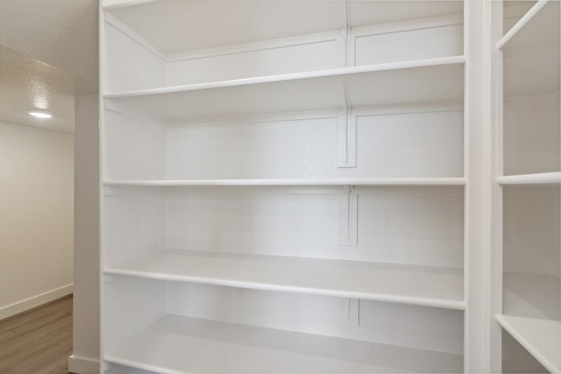 A white, minimalist shelving unit with multiple empty shelves, situated in a bright, neutral-toned room.