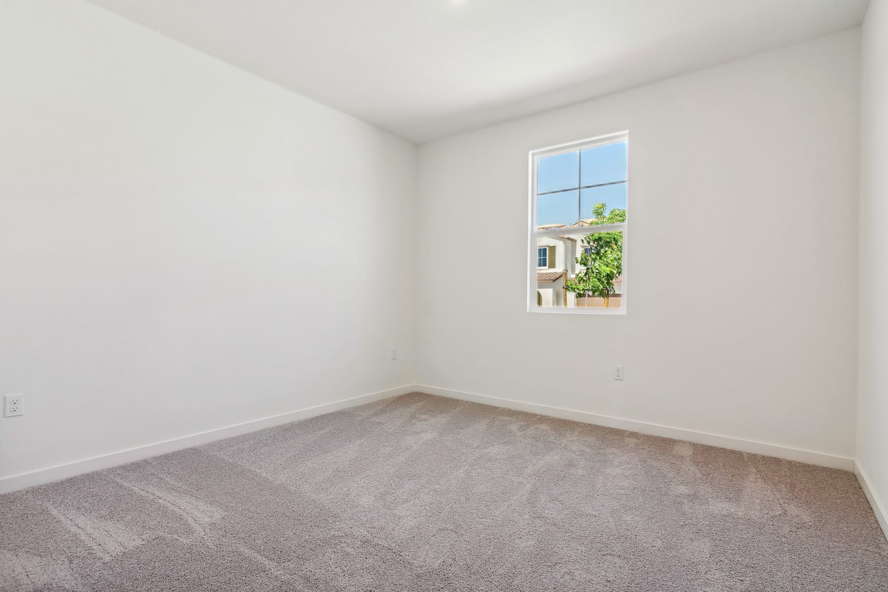 A bright, empty room with a window overlooking a lush, green outdoor scene.