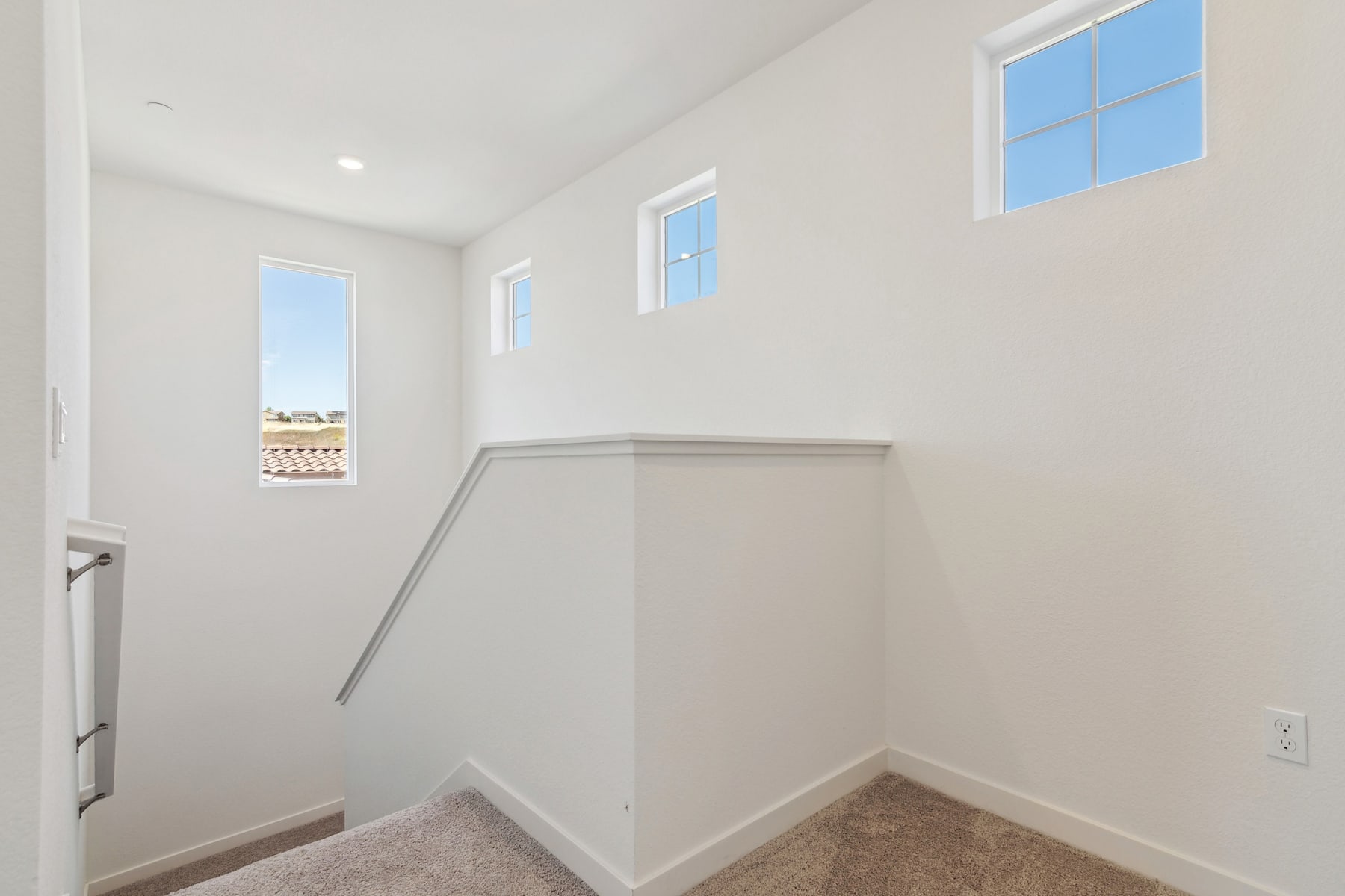 A bright, open stairwell with white walls, a carpeted floor, and several windows providing natural light.