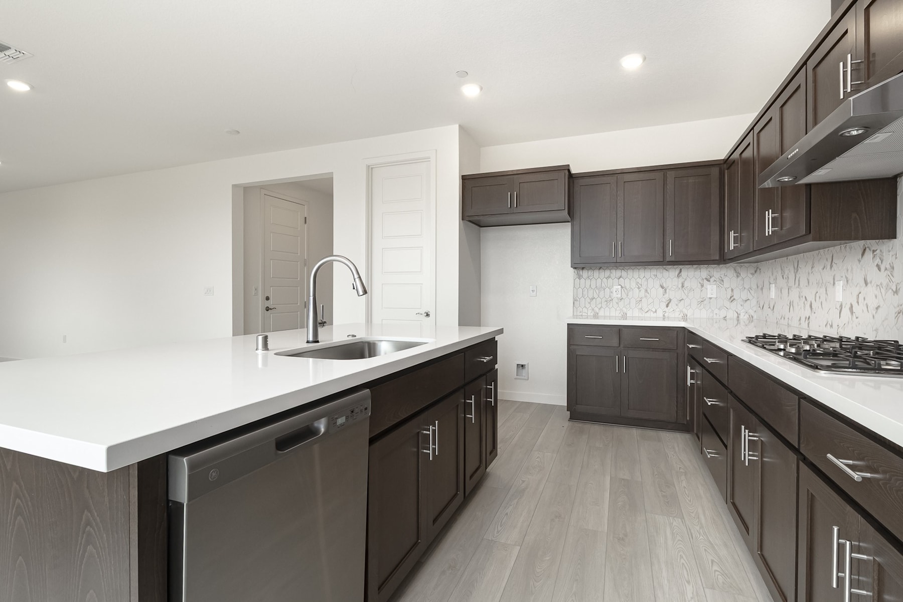 A modern, well-equipped kitchen with dark wood cabinets, white countertops, and a tiled backsplash, set against a bright and airy background.