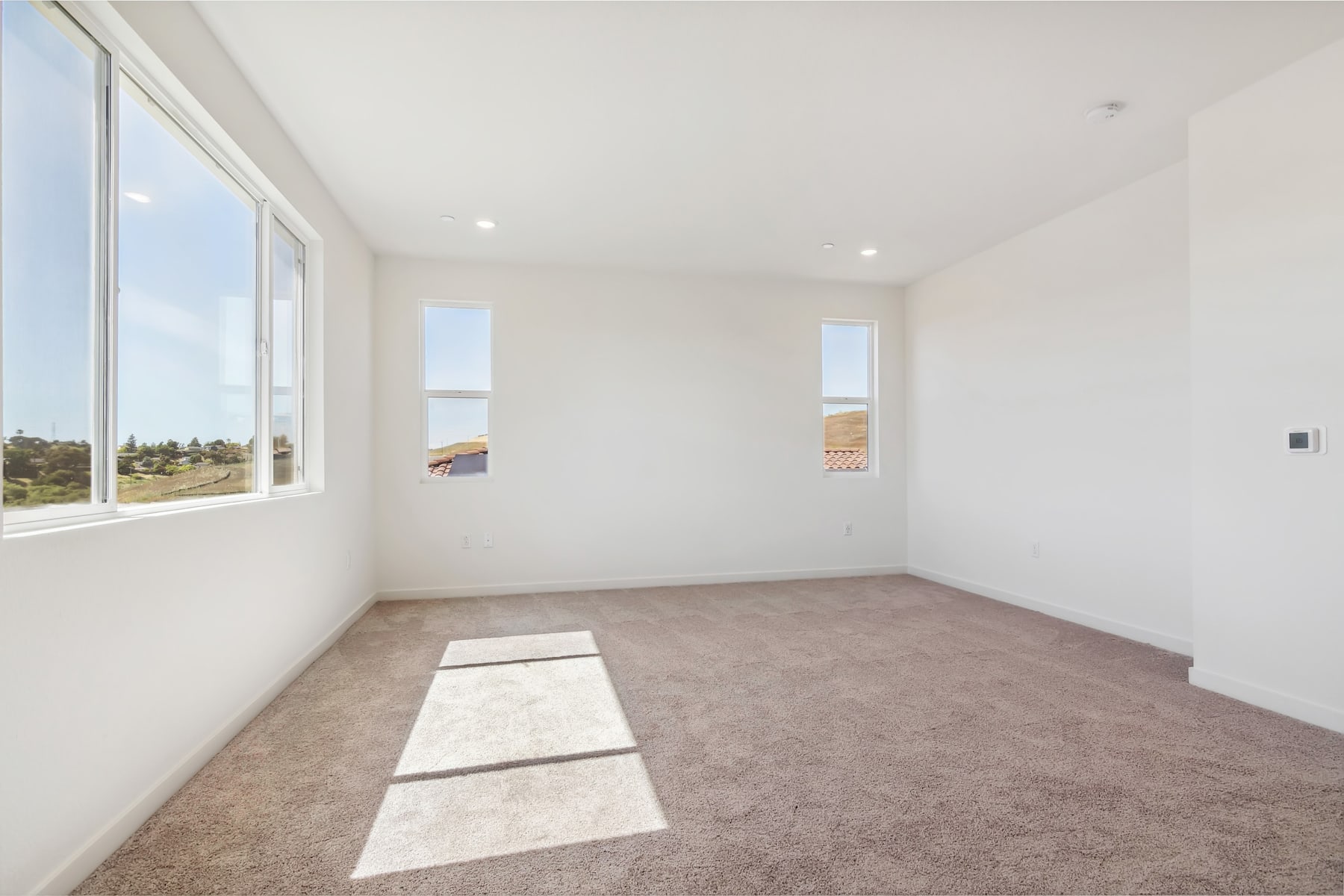 A spacious, well-lit room with large windows overlooking a scenic outdoor landscape, featuring a carpeted floor and a simple, minimalist interior design.