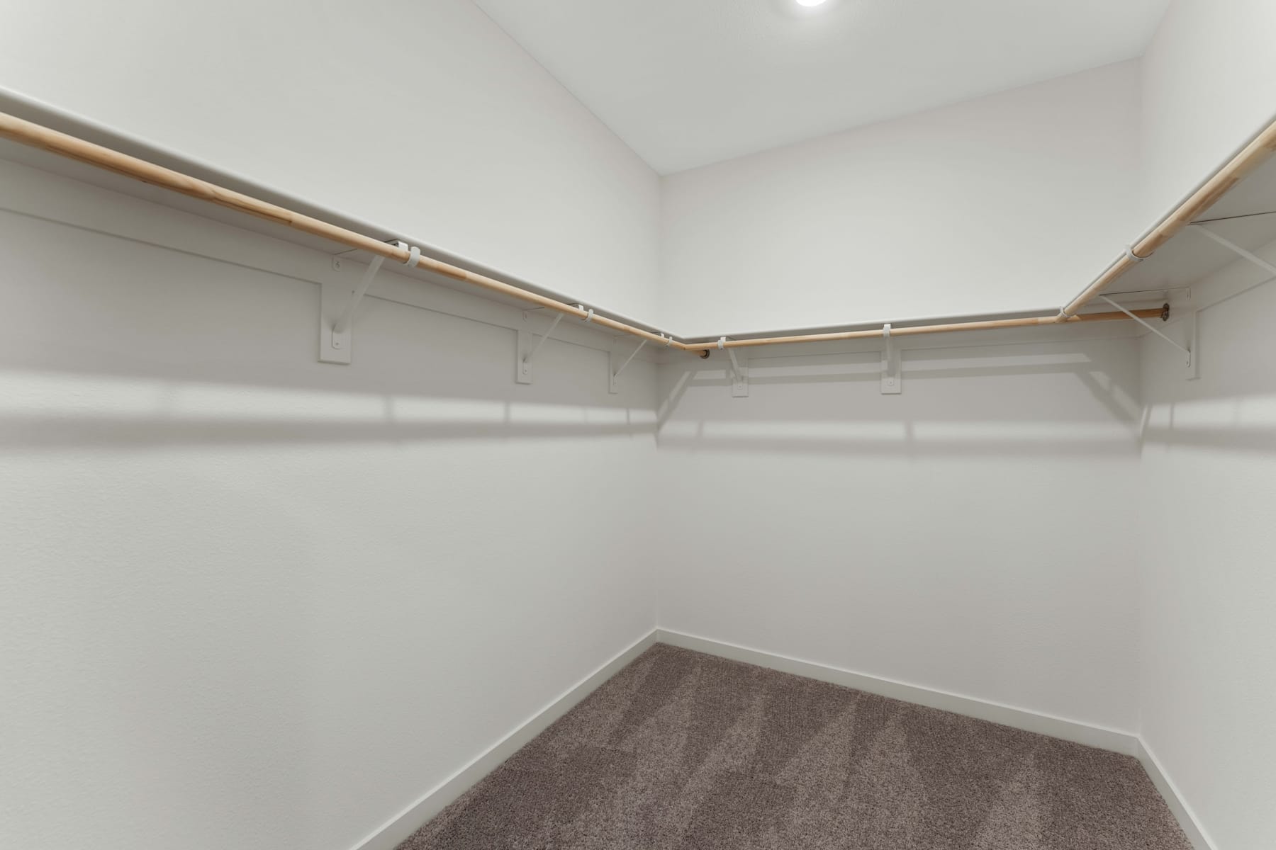 A spacious, well-lit closet with white walls, wooden hanging rods, and a carpeted floor.
