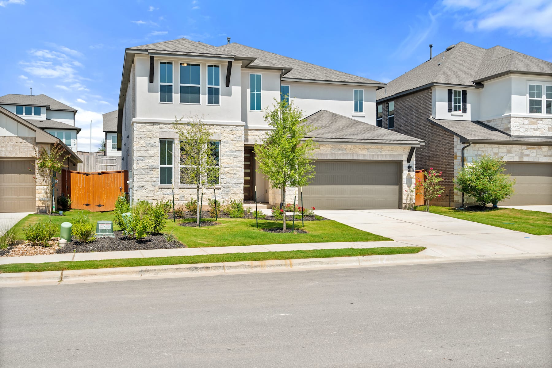 A two-story residential house with a stone exterior, surrounded by a well-manicured lawn and landscaping, situated in a suburban neighborhood.