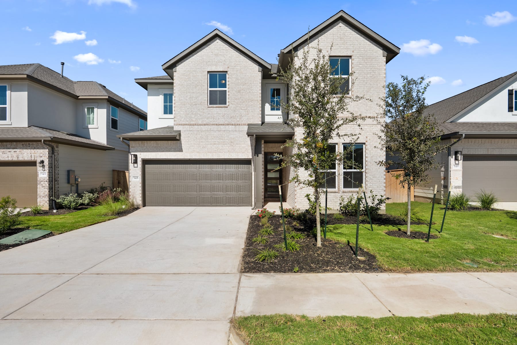 A modern two-story residential building with a gray exterior, a garage, and a well-maintained lawn in the foreground, set against a clear blue sky with some clouds.